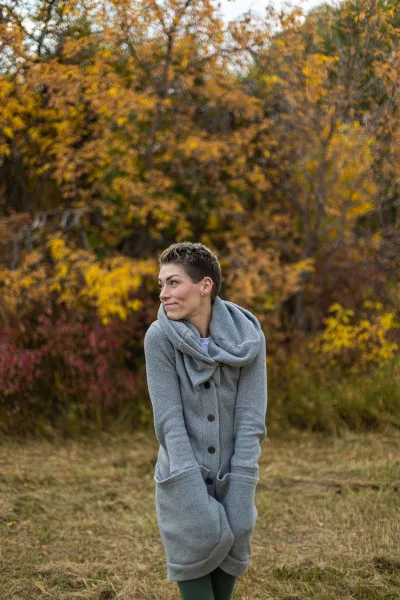 Portrait photo of a woman in a grey sweater standing outside near some trees