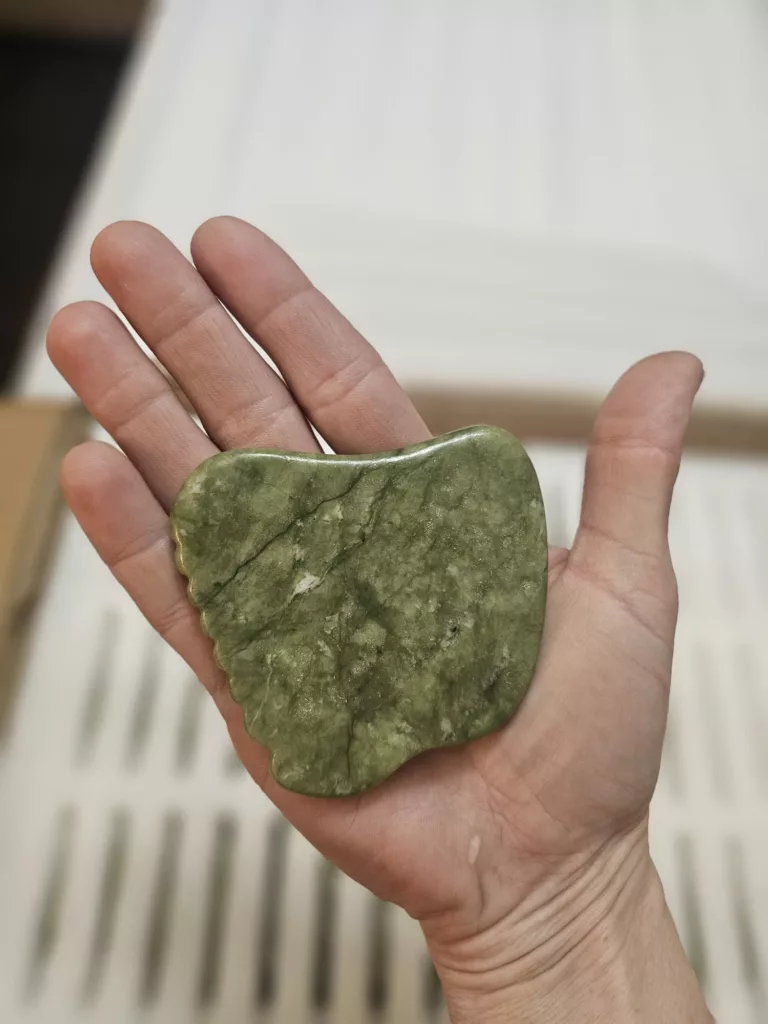 Hand holding a single Vavatu Jade Gua Sha Stone on a flat white surface