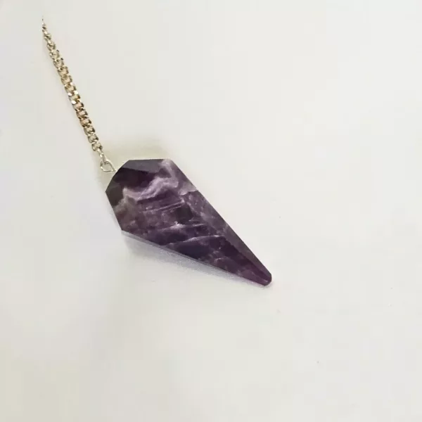 Vavatu Amethyst Crystal Pendulum is shown. The color is purple, and it is a 6 faceted diamond shaped. The crystal pendulum is in the center of the photo with a white backdrop and a single thin gold chain attached to the larger circular end.