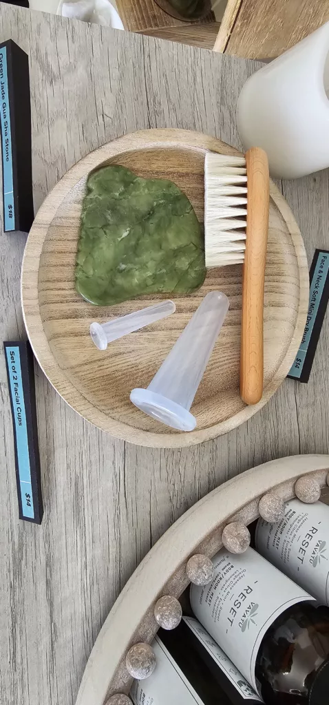 Gua sha jade green stone, facial brush, silicone face cupping devices on a wood plate